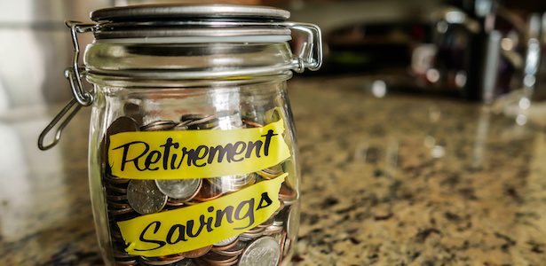 Retirement Savings Money Jar. A clear glass jar filed with coins and bills, saving money. The words "Retirement Savings" written on the outside.